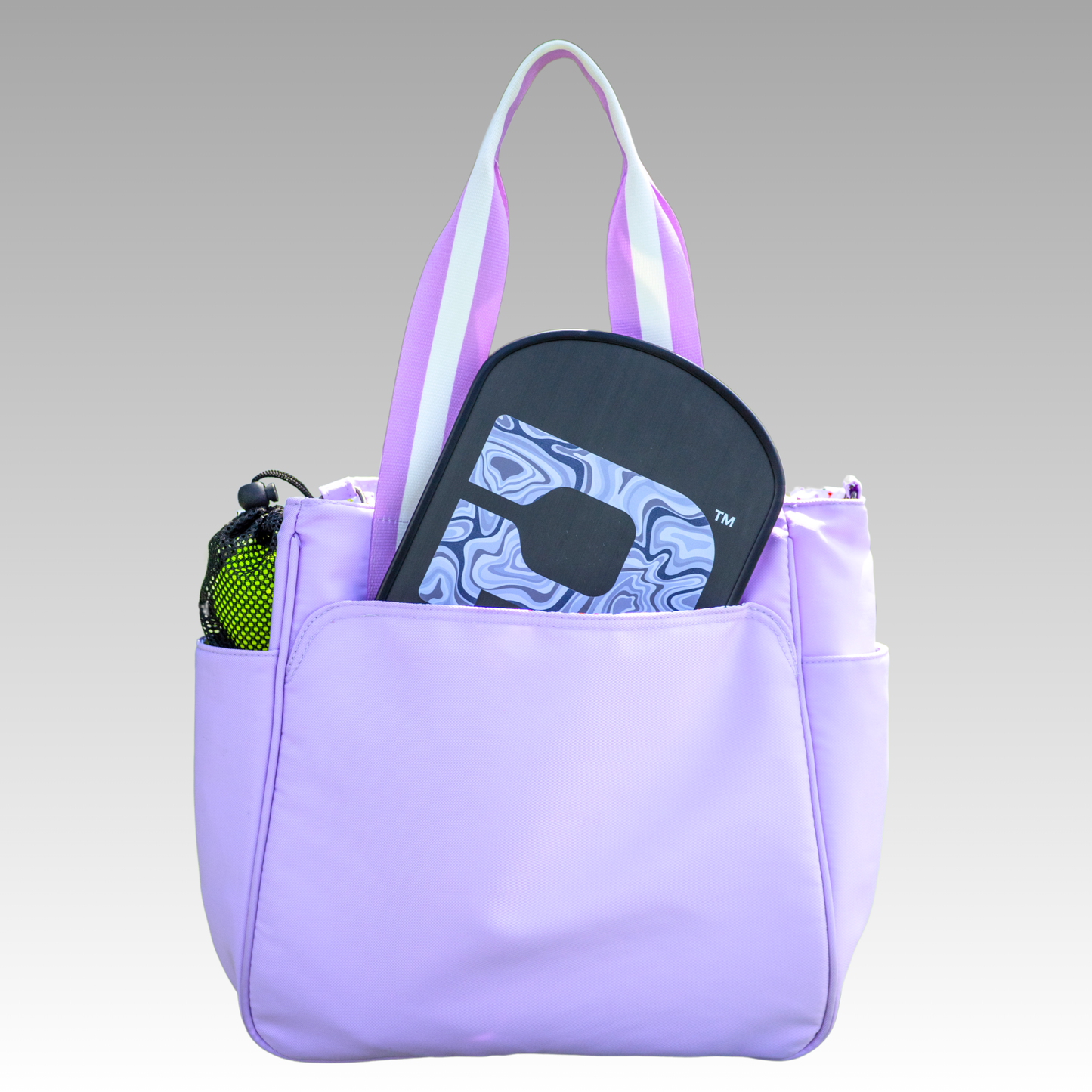 Purple tote bag with a black paddle and pickleball balls inside on a gray background
