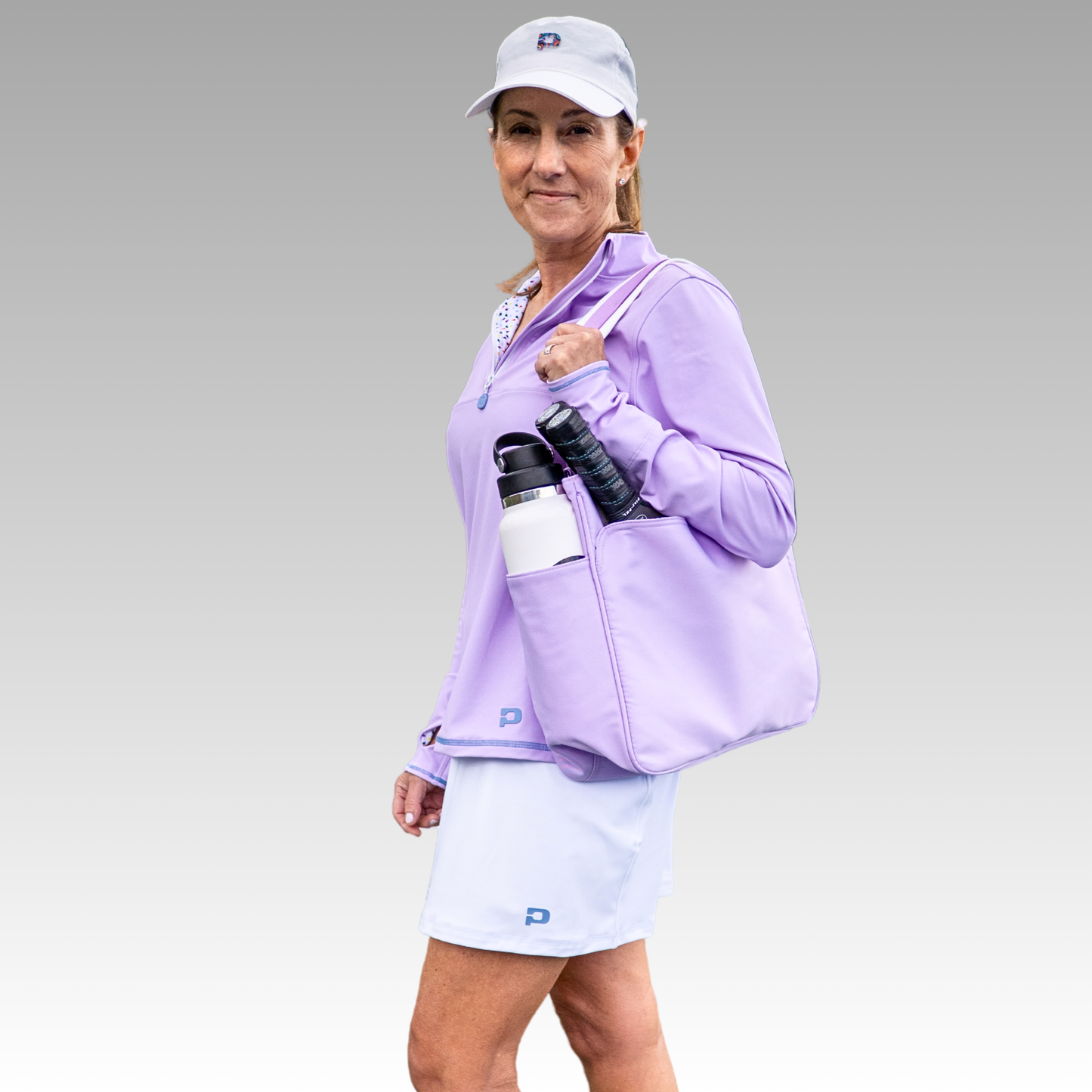 Woman in a purple jacket and white cap holding a bag with water bottle on a gray background