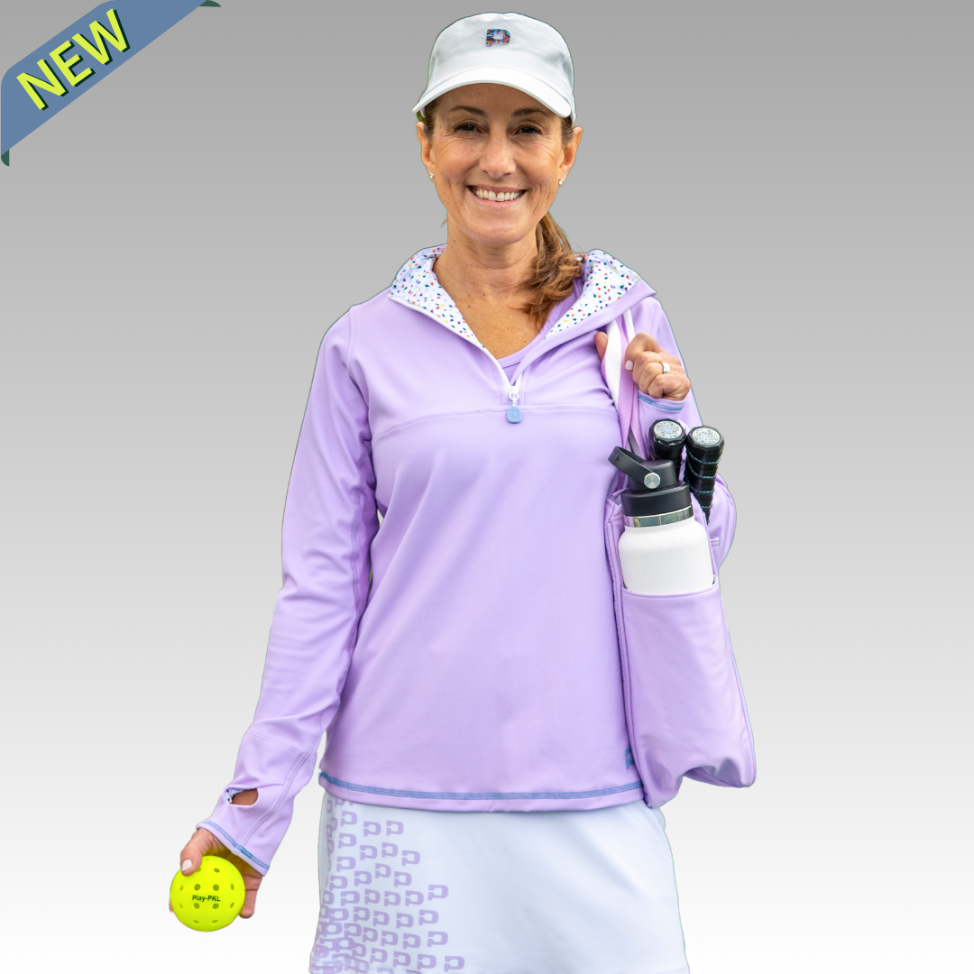 Woman in purple pickelball outfit holding a Lulu pickleball tote with a water bottle in the pocket and holding a pickleball against a gray background